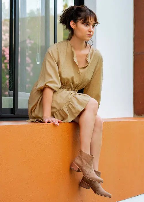 A woman wears beige dress with ankle cowboy boots
