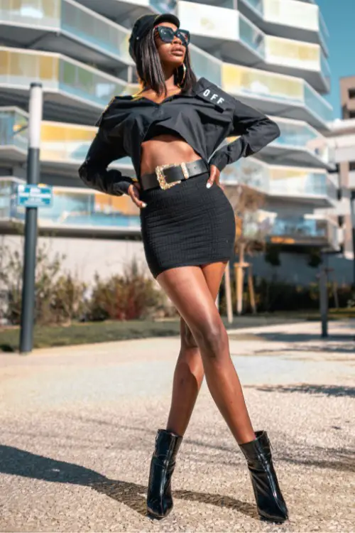 A woman wears black ankle cowboy boots with a black skirt and a crop top