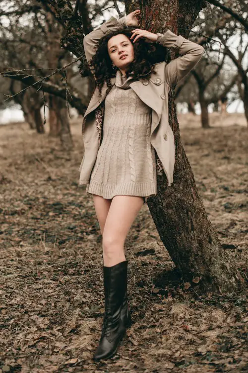 A woman wears black boots with sweater dress and a blazer