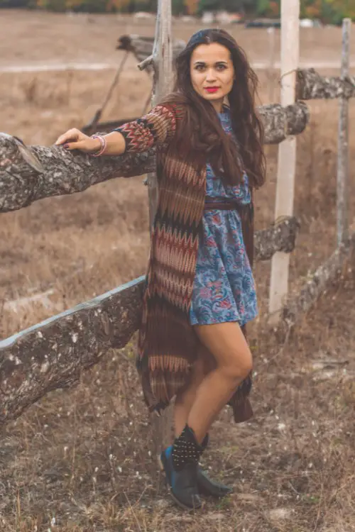 A woman wears black cowboy boots with a floral dress an a coat