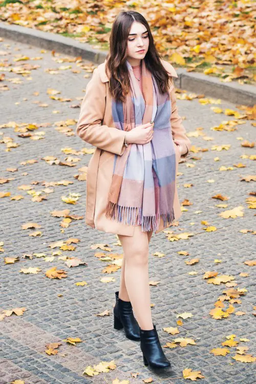 A woman wears black cowboy boots with trench coat and a scarf