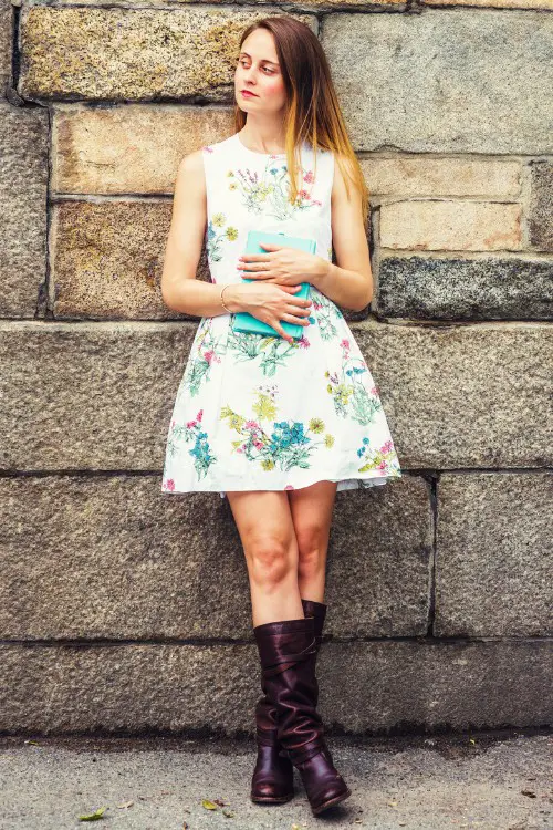 A woman wears bright floral dress with cowboy boots