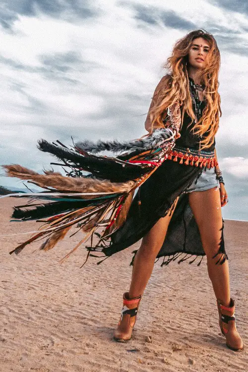 A woman wears brown ankle cowboy boots with a denim short and an boho top