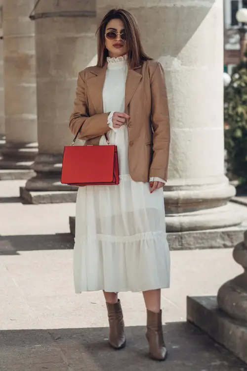 A woman wears brown cowboy boots with a white dress and a blazer