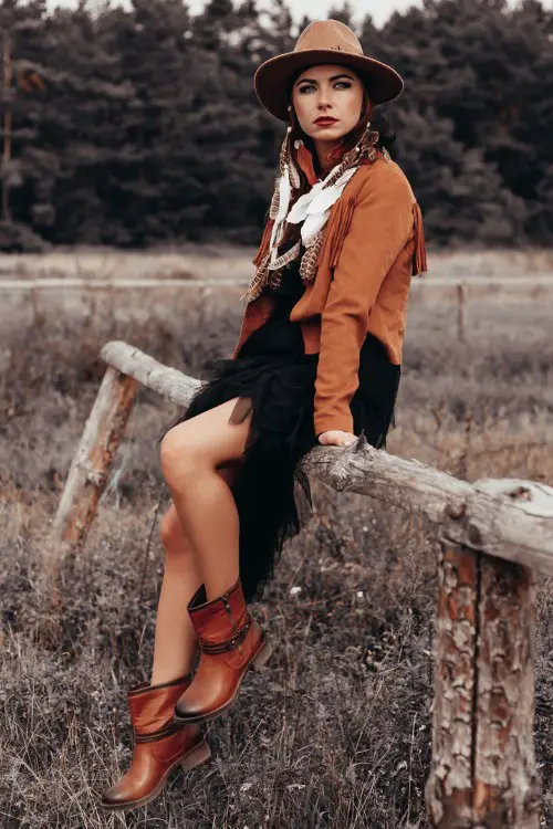 A woman wears brown cowboy boots with black dress and brown coat