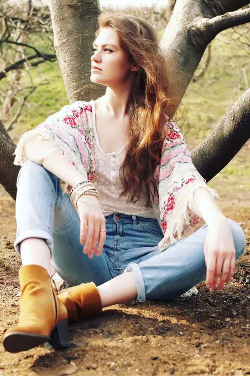 A woman wears brown cowboy boots with jeans, boho coat and a light top