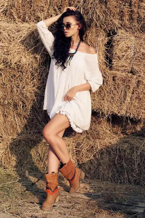 A woman wears brown cowboy boots with white dress on the ranch