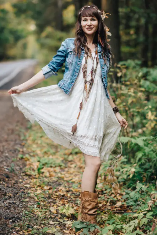 A woman wears cowboy boots with a denim jacket and a lace dress