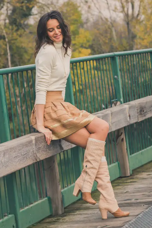 A woman wears cowboy boots with a turtleneck and a skirt