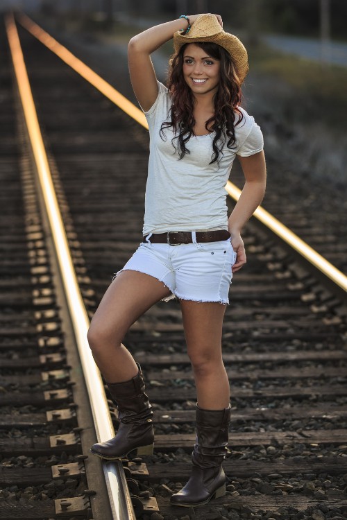 A woman wears cowboy boots with denim shorts, light top and a cowboy hat