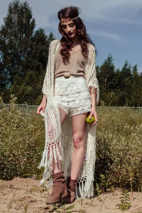 A woman wears cowboy boots with lace shorts, beige top and a light coat