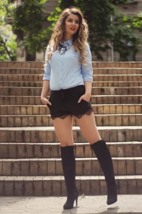 A woman wears cowboy boots with shorts and a shirt