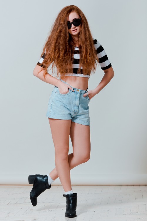 A woman wears cowboy boots with shorts and a striped shirt