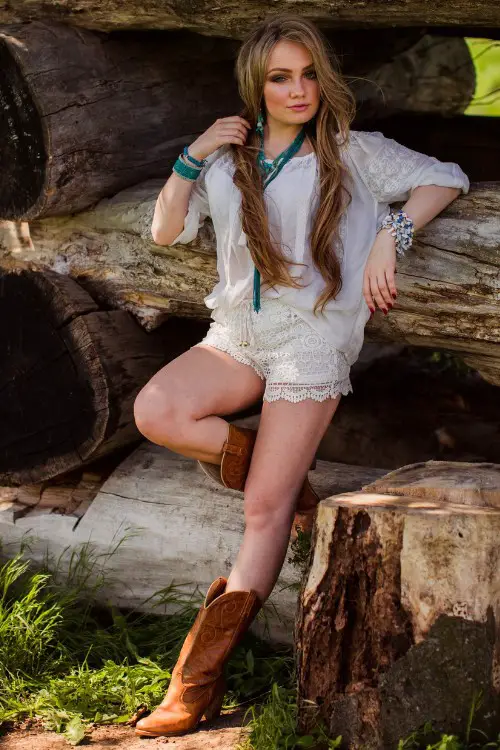 A woman wears cowboy boots with white shorts and a shirt