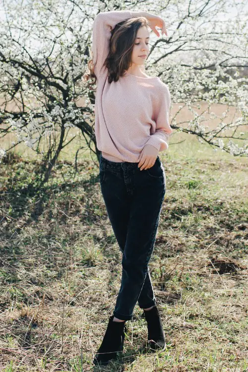 A woman wears dark jeans, sweater and a pair of black ankle cowboy boots