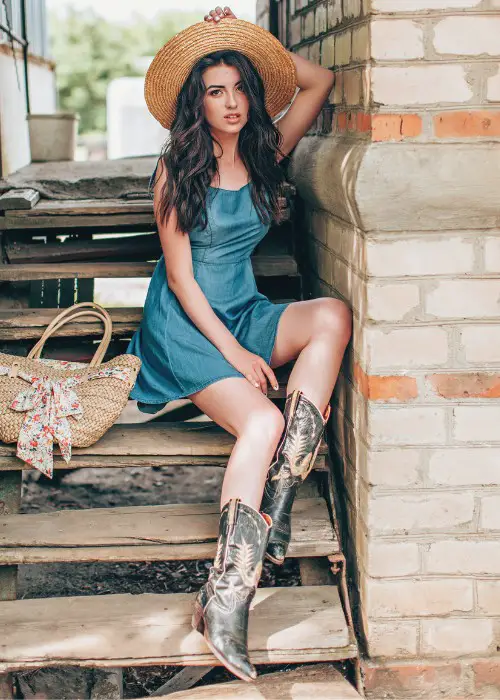 A woman wears denim dress with cowboy boots