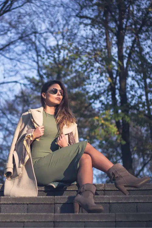 A woman wears fitted dress with long coat and grey cowboy boots