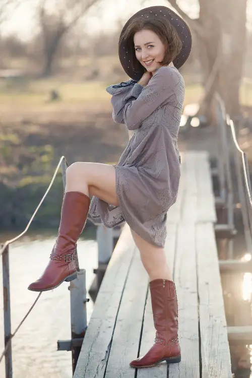 A woman wears grey dress with brown cowboy boots