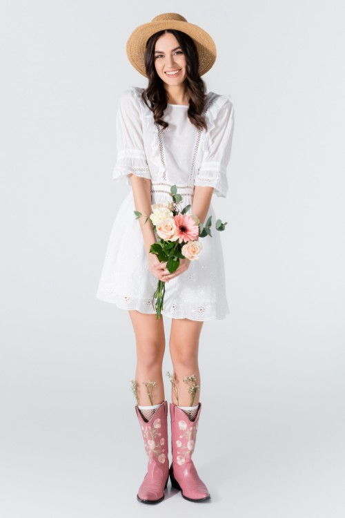 A-woman-wears-pastel-pink-cowboy-boots-with-a-white-dress-and-a-cowboy-hat