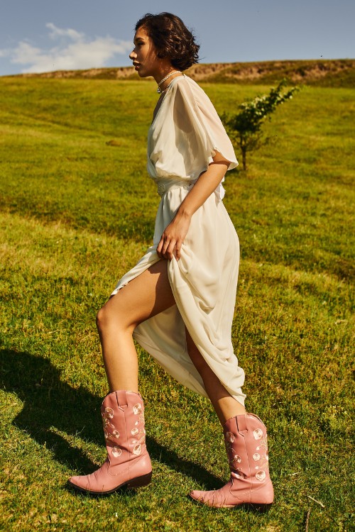 A woman wears pink cowboy boots with a white dress