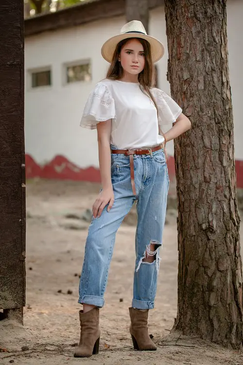 A woman wears ripped jeans with suede cowboy boots and a white top