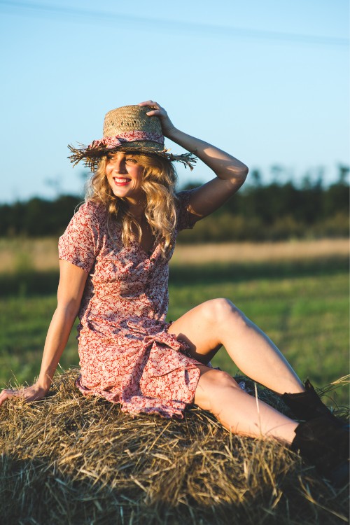 A woman wears straw hat with a floral dress and a pair of cowboy boots