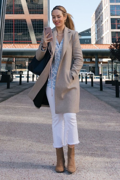 A woman wears suede cowboy boots with ripped hem jeans and a long blazer