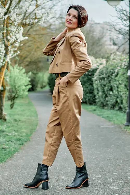 A woman wears tan suit with black ankle cowboy boots