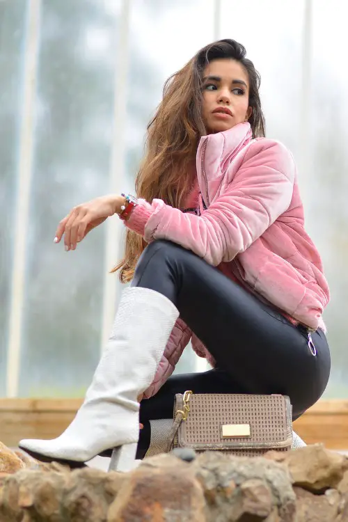 A woman wears white cowboy boots with leggings and pink coat