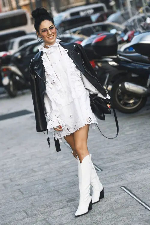 A woman wears white cowboy boots with white dress and black coat