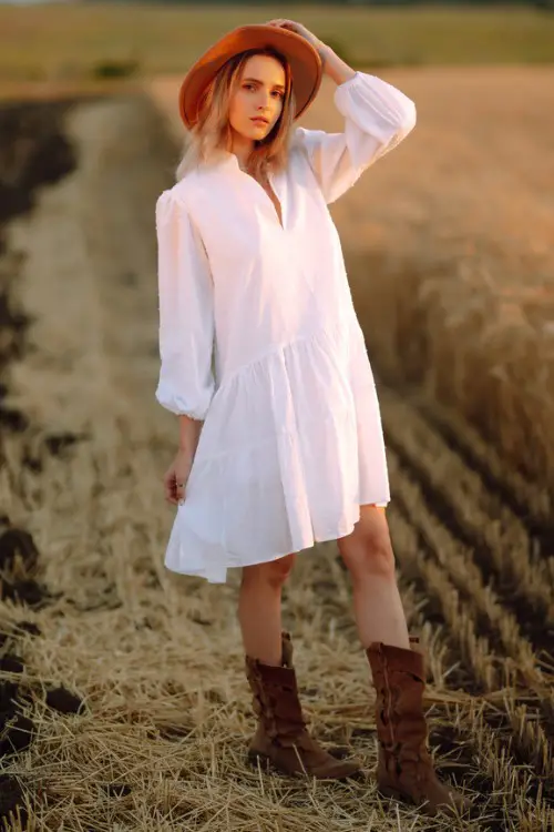 A woman wears white dress, cowboy boots and a cowboy hat