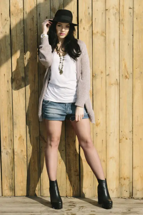 a woman wears shorts with ankle cowboy boots and cardigan