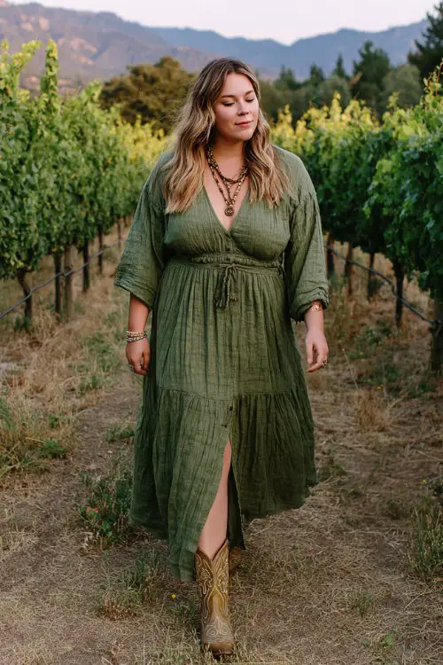 A plus-size woman wears a flowy green maxi dress with a subtle slit and gathered waist, styled with embroidered cowboy boots