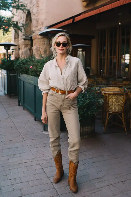 A woman over 30 wears high-waisted straight-leg jeans with a tucked-in soft linen blouse and tan cowboy boots