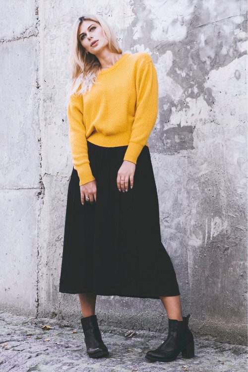 A woman wears a black skirt, yellow sweater and black cowboy boots