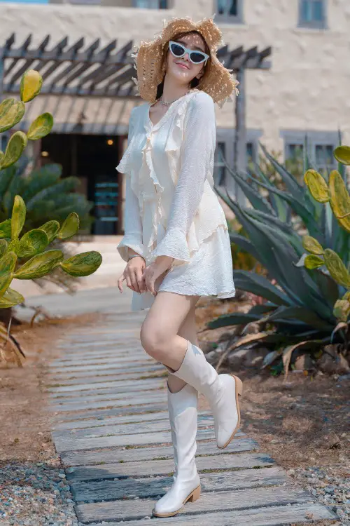 A woman wears cream cowboy boots with a dress.