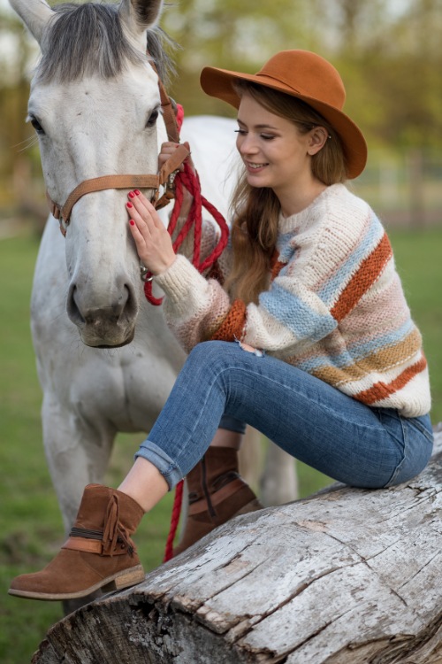 A woman wears ankle suede cowboy boots with jeans and a sweater and a wide brimmed hat