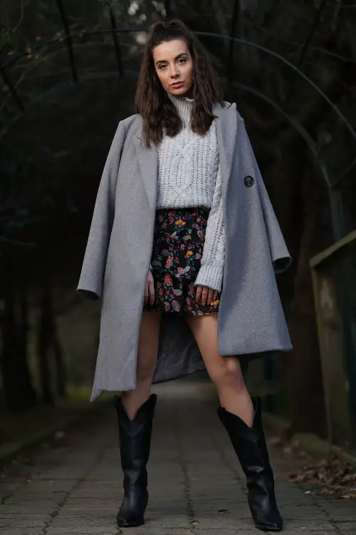 A woman wears black cowboy boots, black floral dress and a sweater