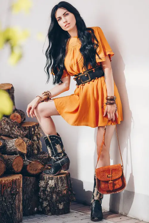 A woman wears cowboy boots with orange dress