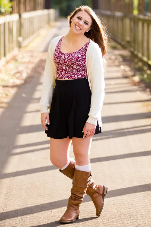 A woman wears brown cowboy boots with a black skirt and a floral top with light cardigan