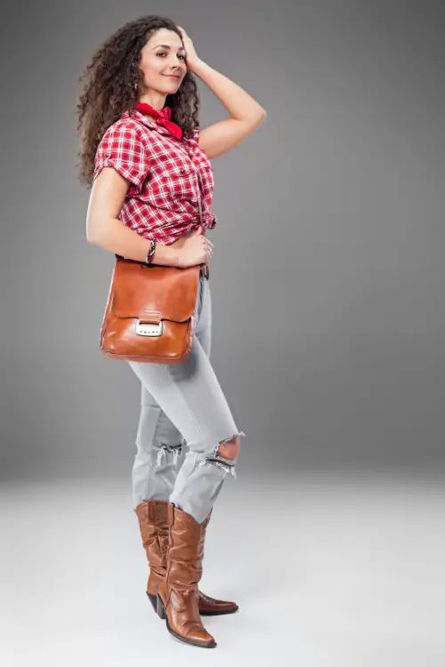 A woman wears ripped jeans with brown cowboy boots and a plaid top