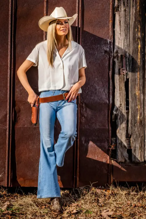 A woman wears brown cowboy boots with a white top , cowboy hat