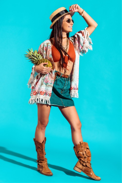 A woman wears cowboy boots withsa skirt and a boho cardigan