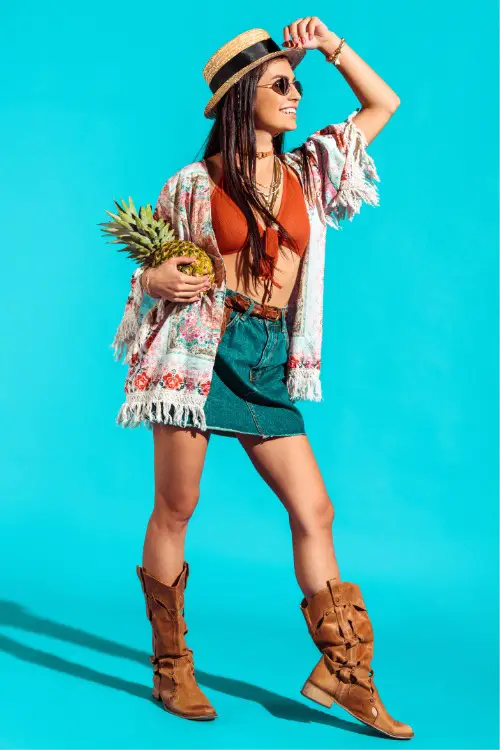 A woman wears cowboy boots withsa skirt and a boho cardigan