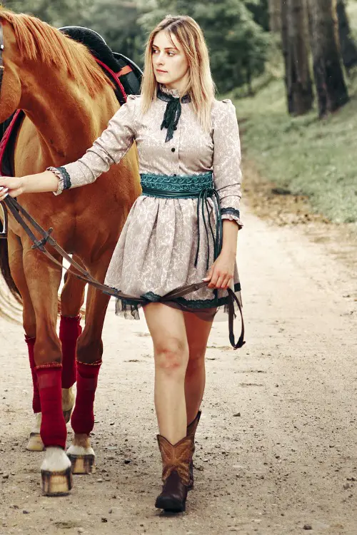 A woman wears cowboy boots with a beige dress