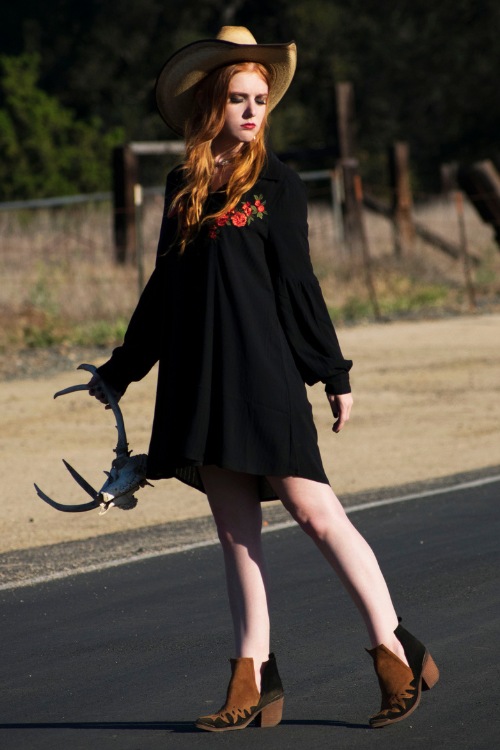 a woman wears cowboy boots with a black dress and a cowboy hat