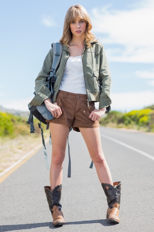a woman wears cowboy boots with brown shorts, white top and a jacket