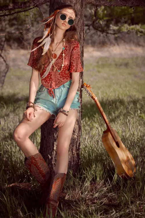 A woman wears cowboy boots with a denim short and a boho top