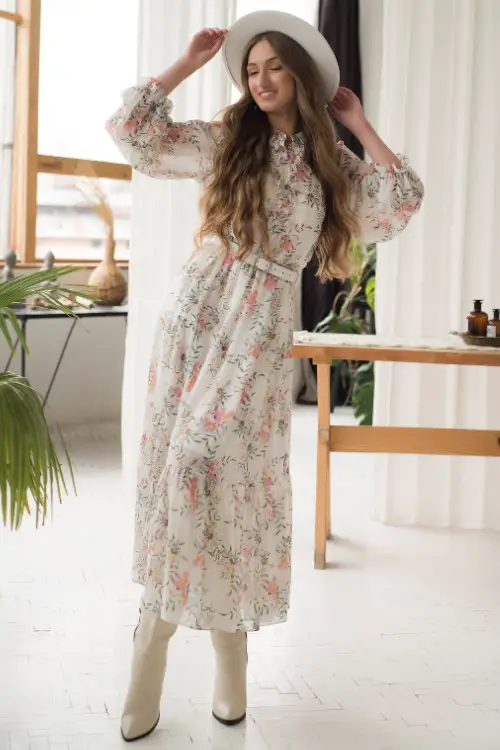 A woman wears cowboy boots with a floral dress and a white cowboy hat