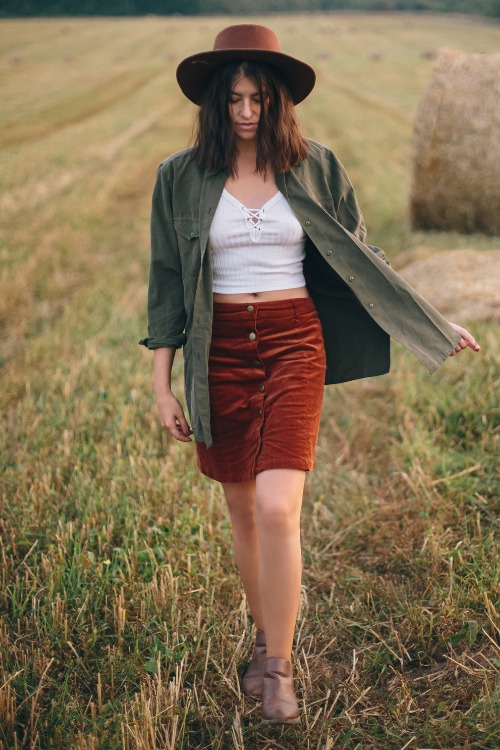 A woman wears cowboy boots with a red skirt, mini white top and an olive coat